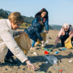 Group of female volunteers picking up trash on the beach. Selective focus on woman in foreground