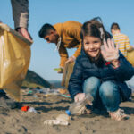 Little happy girl with volunteers picking up trash on the beach
