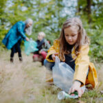 A small girl with mother and grandmother picking up waste outoors in forest.