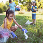 Portrait of little girl, volunteer picking up trash in the park. Saving environment.
