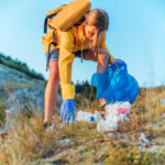 Young caucasian woman activist picking up trash in nature